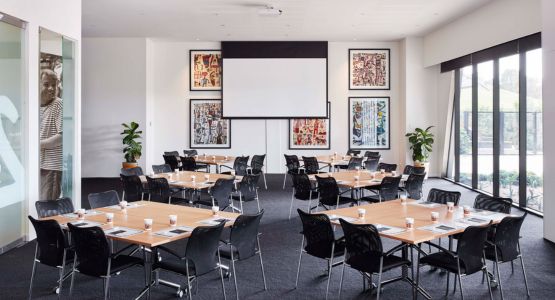 A meeting venue with four square desks and a projector screen